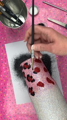 someone is painting hearts on a piece of paper with glitter and a pen in their hand