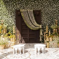 an outdoor wedding setup with flowers and greenery on the wall behind two white tables