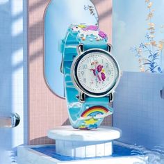 a blue watch sitting on top of a white pedestal in front of a mirror and tiled wall