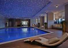 a large indoor swimming pool with lounge chairs next to it and lights on the ceiling