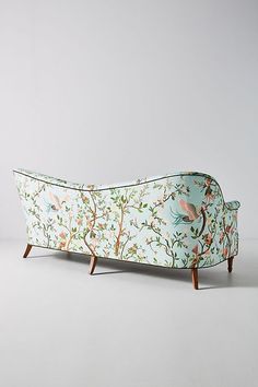 an upholstered couch with birds and flowers on the back, against a gray background