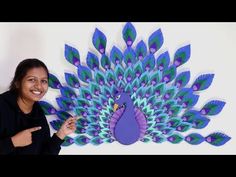 a woman pointing at a paper peacock on the wall