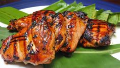 two pieces of grilled meat sitting on top of a white plate next to green leaves