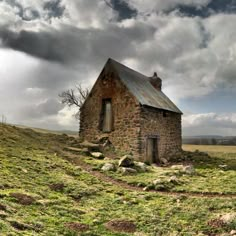 an old stone building sitting on top of a lush green hillside under a cloudy sky