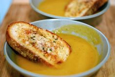 two bowls filled with soup on top of a wooden table next to a sandwich cut in half