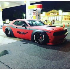 a red and gray car is parked in front of a gas station at night time