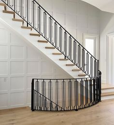 a staircase with black railing and wooden flooring in a white room next to an open door