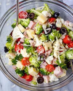 a salad with broccoli, tomatoes, olives and ham in a glass bowl