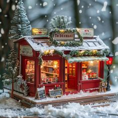 a small red store with christmas decorations on the roof and trees in the snow outside