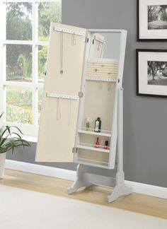 a white jewelry cabinet with an open door on the side and shelves below it, in front of a gray wall