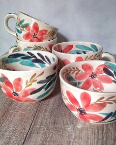 four bowls with painted flowers on them sitting on a wooden table next to each other