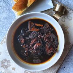 a bowl of beef stew with bread on the side