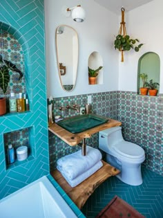 a bathroom with blue tiles and green tile on the walls, including a wooden shelf