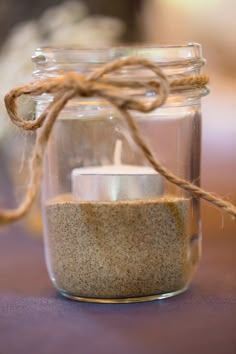 a candle in a glass jar with twine on the handle and rope around it