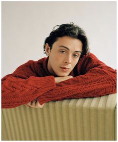 a young man in a red sweater leaning on a radiator with his arms crossed