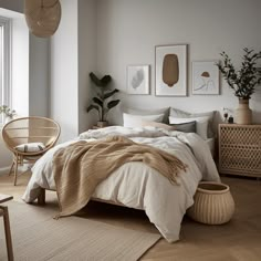 a bedroom with white walls and wooden flooring has a large bed, wicker chair, potted plant on the far side