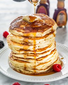 a stack of pancakes with syrup being drizzled over them and topped with raspberries