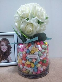 a vase filled with white roses next to a framed photo and some candies in it