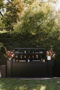 an outdoor bar set up in the middle of a yard with flowers and bottles on it