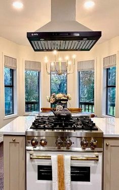 a kitchen with an oven, stove and two windows in the room that has curtains hanging from the ceiling