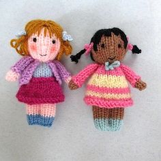 two crocheted dolls sitting next to each other on a white surface with one holding the hand of another doll