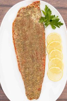 a white plate topped with fish next to lemons and parsley on top of a wooden table