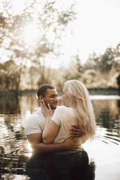 a man and woman standing in the water with their arms around each other looking at each other