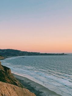 the beach is next to an ocean and some hills with trees on them at sunset