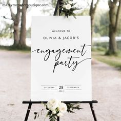 a welcome sign with flowers and greenery is displayed on an easel in front of trees