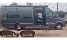 a van with its door open sitting in the parking lot next to some chairs and tables