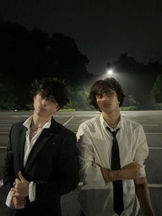 two young men standing next to each other in an empty parking lot at night time