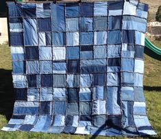 a blue quilt is hanging on a clothes line in the grass with a green slide behind it