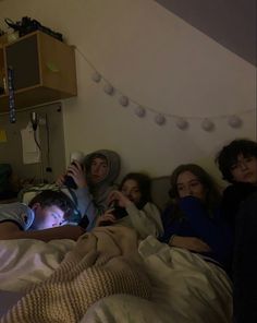 a group of people laying in a bed with one person holding an electronic device up to their face