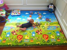 a baby laying on top of a green rug next to a toy car and other toys