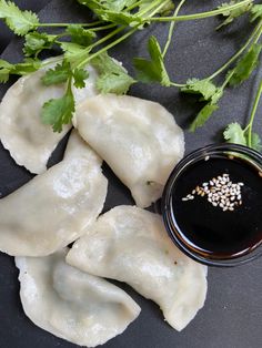 dumplings with dipping sauce and cilantro sprigs next to it on a black plate