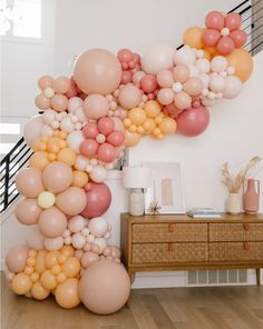 the balloon arch is made up of many different colors and sizes, including pink, orange, yellow, and white balloons