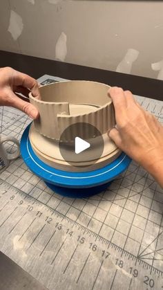 two hands are working on an object that looks like a cup and saucer sitting on top of a table