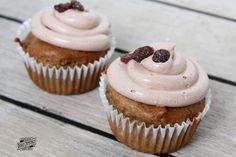 two cupcakes with frosting and raisins sitting on a wooden table