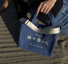 a person sitting in the sand with a blue bag on their lap and one hand holding it