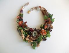 a necklace made out of flowers and leaves on a white surface with an odd looking object in the middle