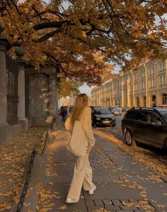 a woman is walking down the street in autumn