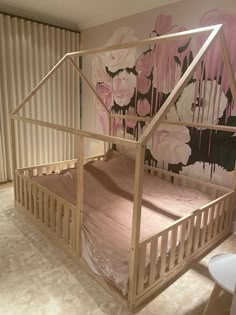 a child's bed with pink flowers painted on the wall behind it, in front of a curtained window