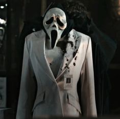 a man in a white suit with a black mask on his face and jacket over his shoulders