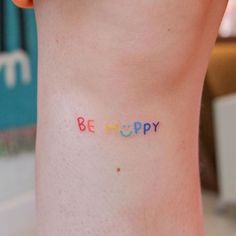 the word be happy written in multicolored letters on the side of a woman's leg