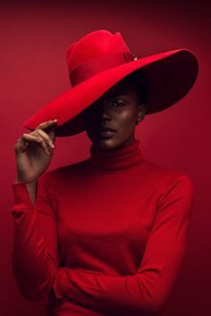 a woman wearing a red hat with her hands on her head and looking at the camera