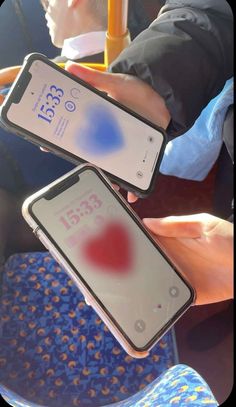 two people holding up their cell phones in front of each other on a train seat