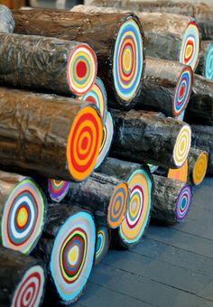 many logs are stacked on top of each other and have colorful circles painted on them