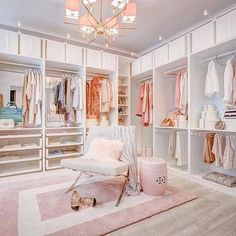 an organized closet with white furniture and pink rug on the floor, chandelier hanging from the ceiling