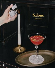 a person holding a lighter next to a drink in a glass on top of a tray