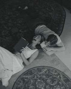 two people laying on the floor next to each other with a book in their hands